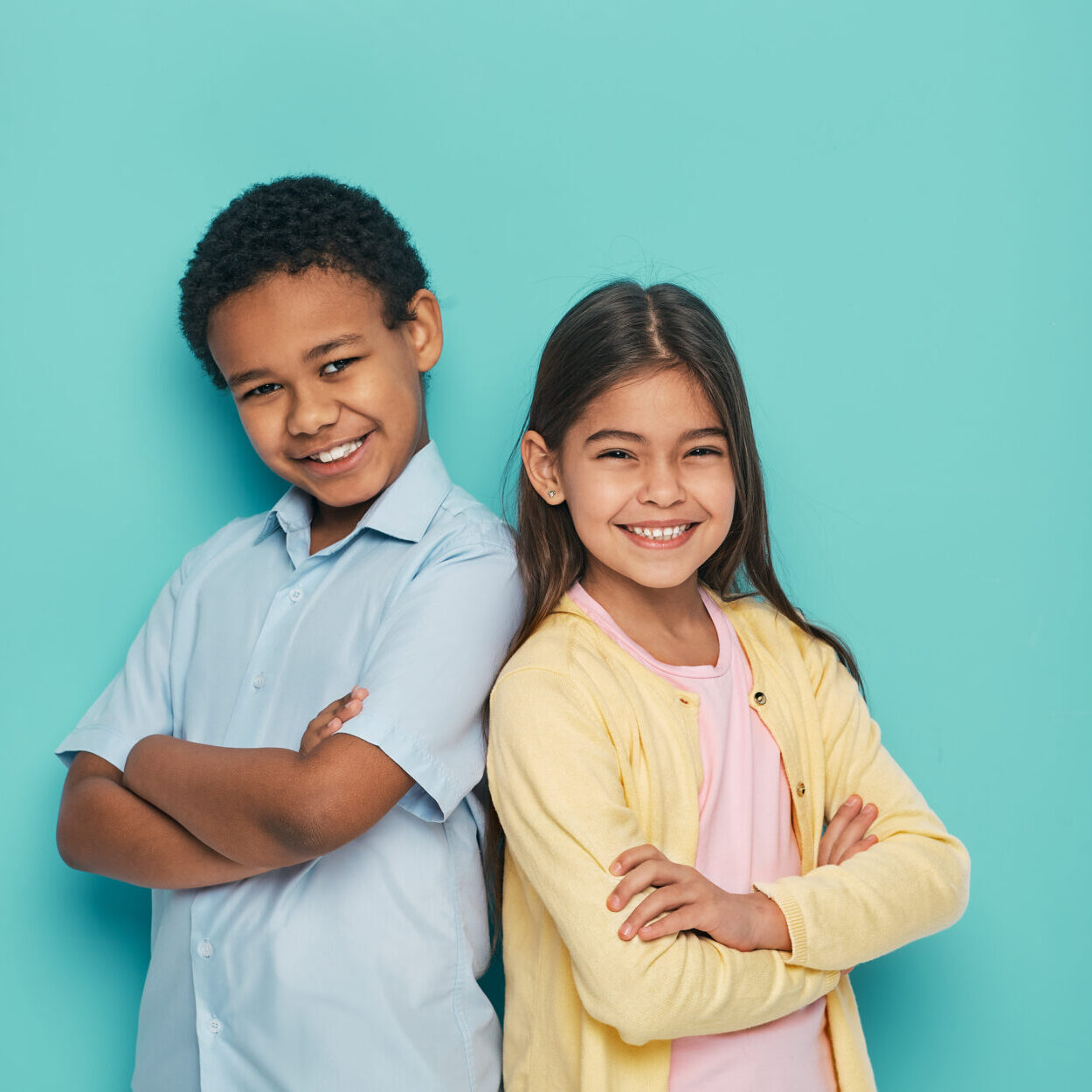 Smiling boy and girl standing confidently with arms crossed against a teal background, representing a friendly atmosphere for pediatric dentistry at Pediatric Dental Partners in Shreveport.